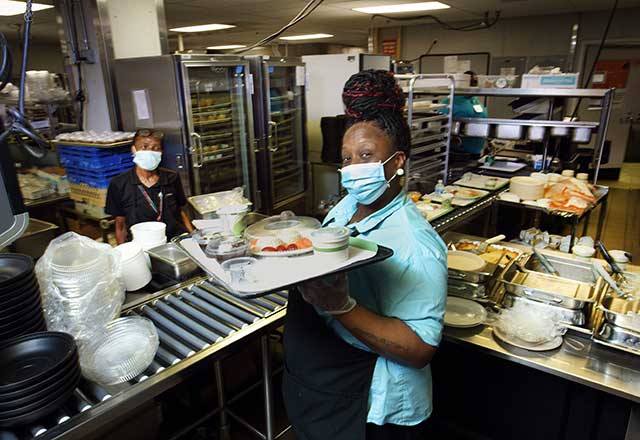 Food service employee wearing a mask with a tray.