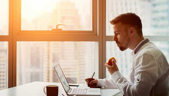 A young man eats an apple while working on his laptop.